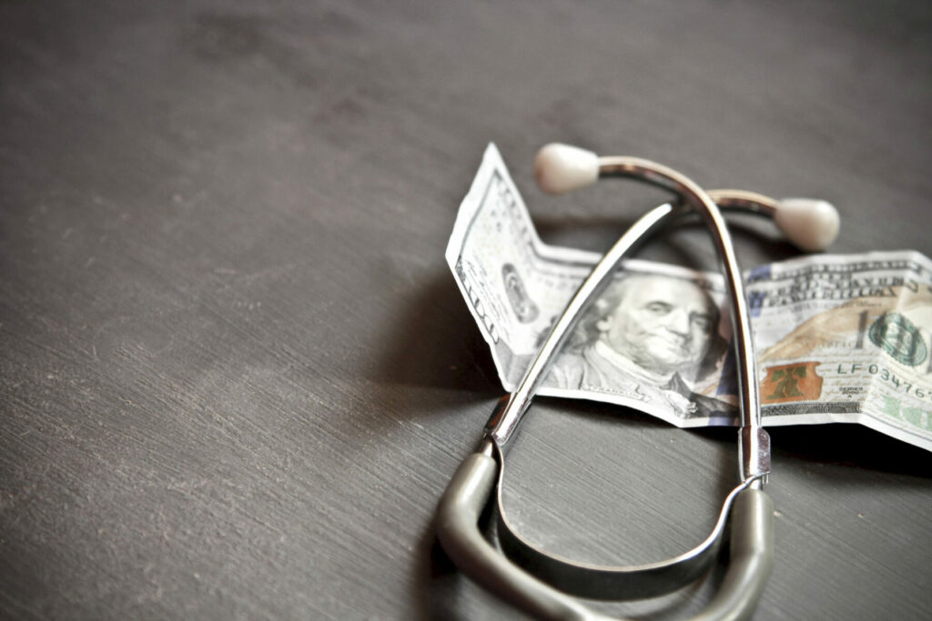 stethoscope sitting on top of a hundred dollar bill