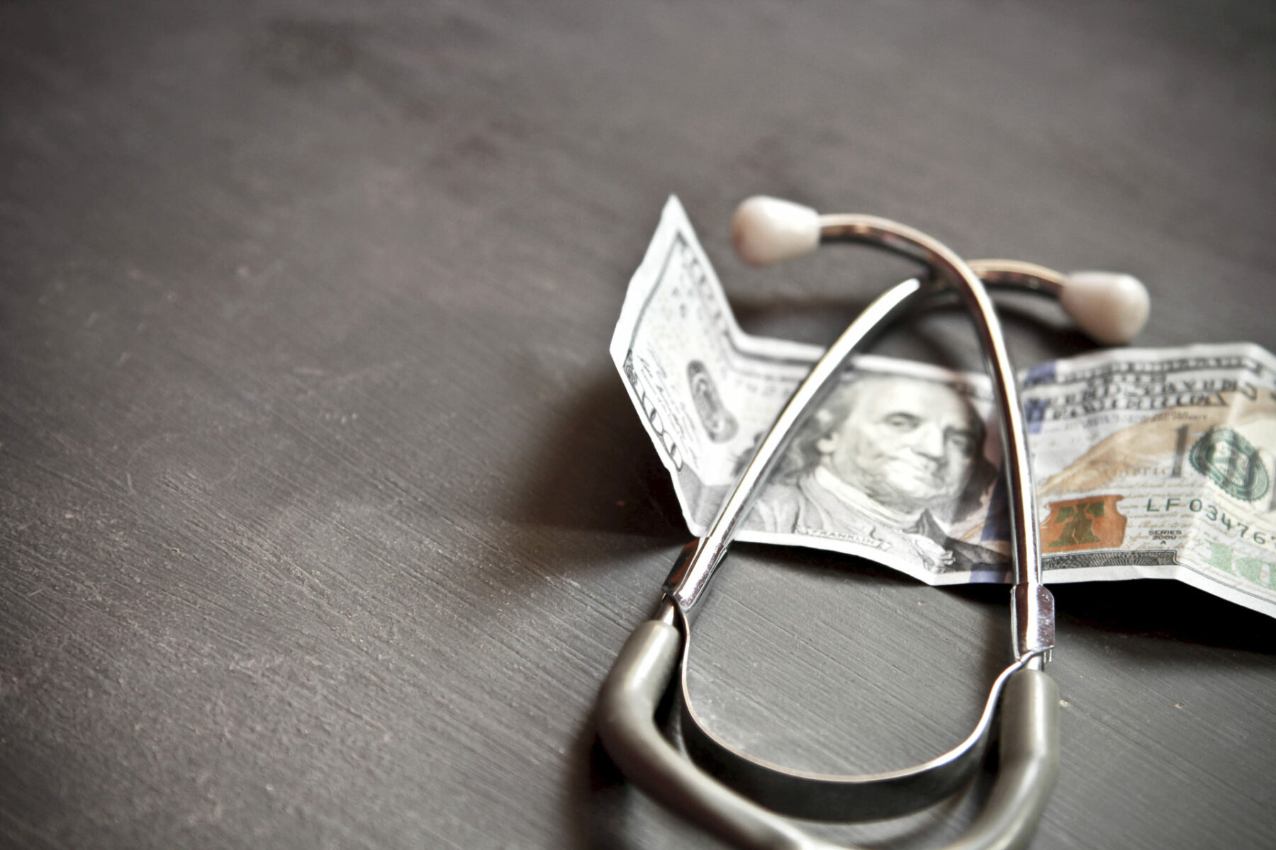 stethoscope sitting on top of a hundred dollar bill