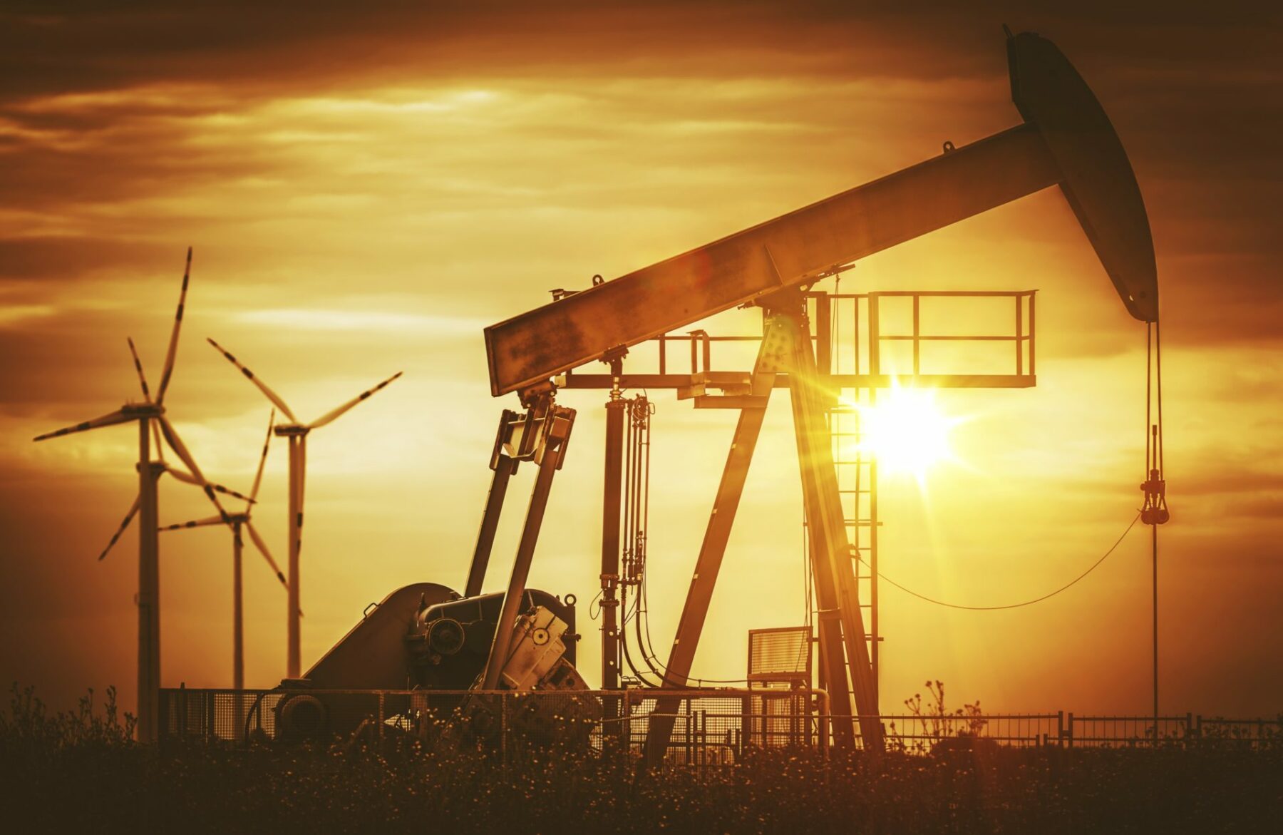 old fashioned oil pump and wind turbines in the background.