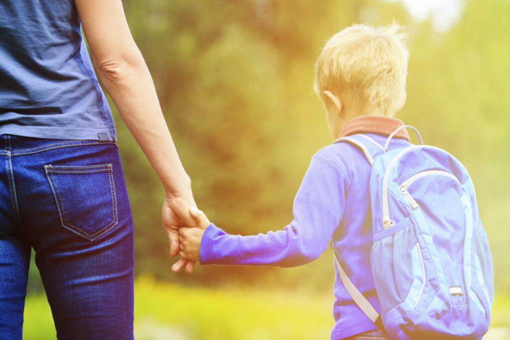 Mother holding hand of little son with backpack outdoors, back to school