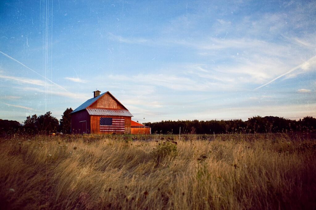 red barn with american flag behind a wheat field