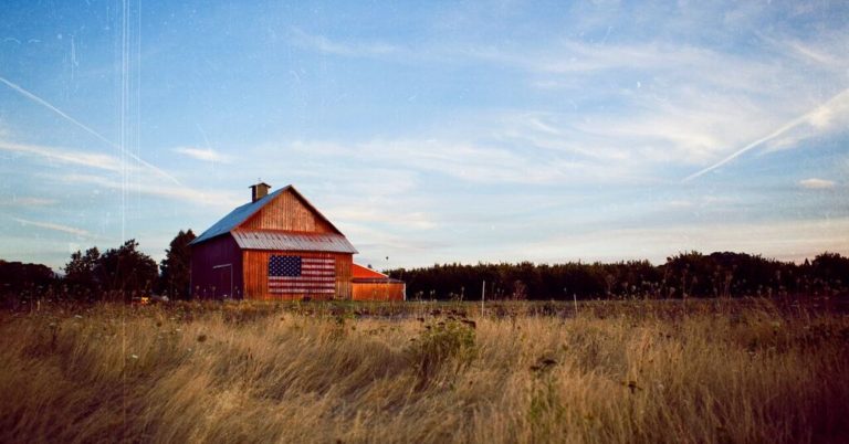 red barn with american flag behind a wheat field