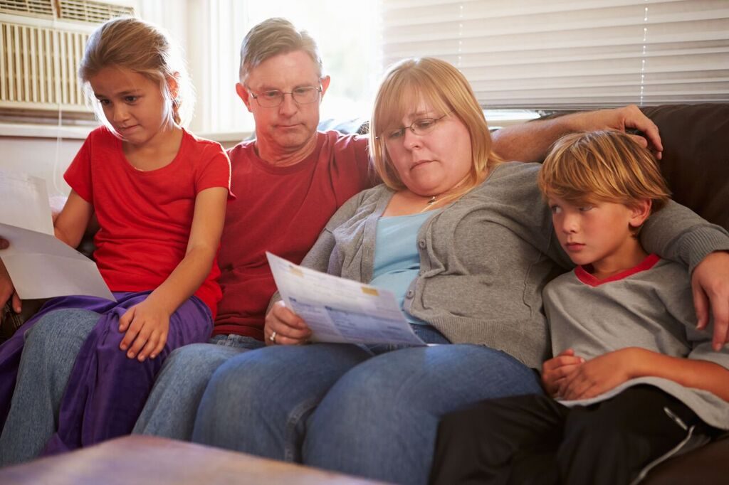 family of four sitting on the couch looking at papers looking worried