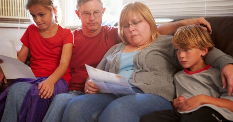 family of four sitting on the couch looking at papers looking worried