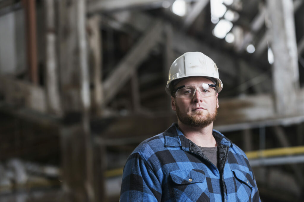 Man wearing hardhat, safety goggles and plaid shirt