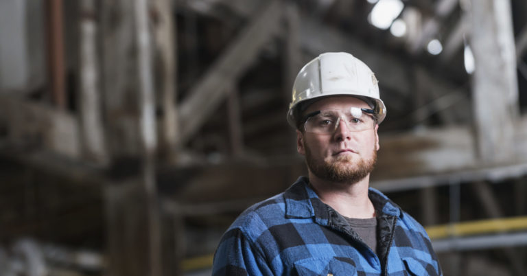 Man wearing hardhat, safety goggles and plaid shirt