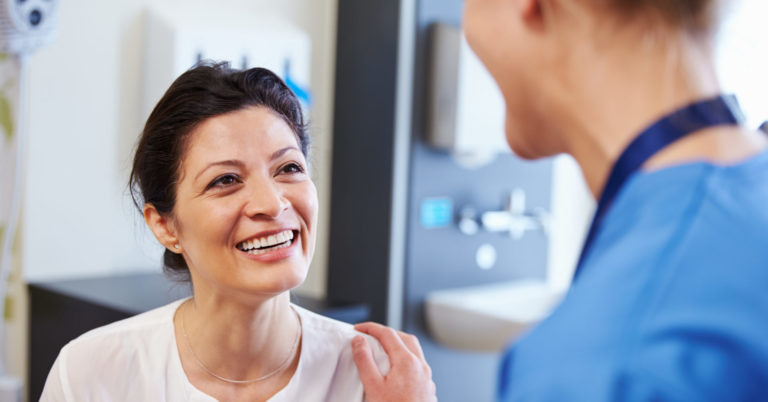 Female Patient Being Reassured By Doctor In Hospital Room