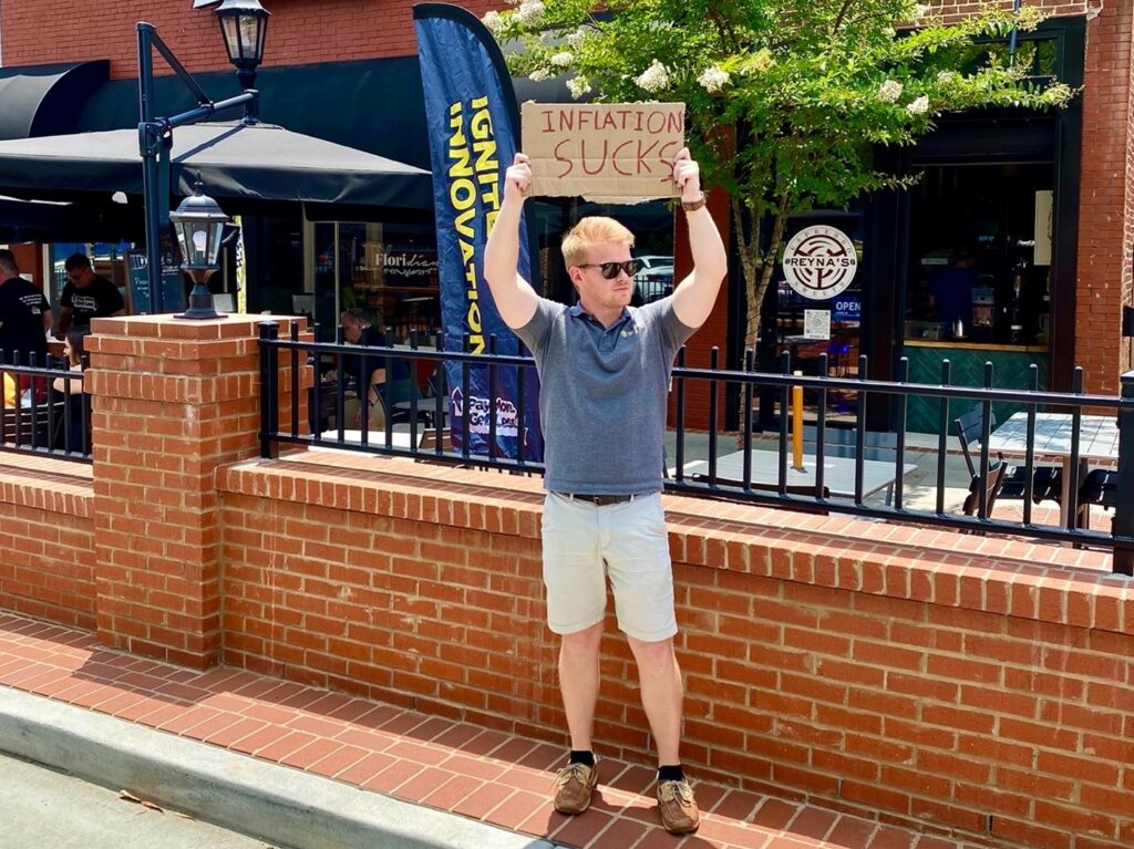 Spencer Evans holds a sign that reads "Inflation sucks" on a stop along AFP's True Cost of Washington Tour to lower prices and connect people to how Washington's wasteful spending is driving historic inflation. 